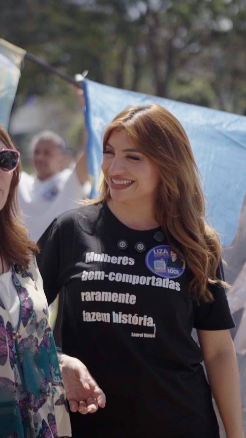 Liza Lopes caminha ao lado de apoiadoras em atividade de rua, sorrindo.