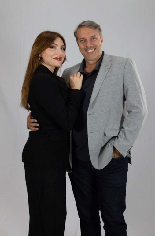 Liza Lopes e Rico Rosas posam juntos, abraçados, em fundo claro de estúdio.