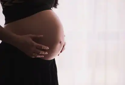 Detalhe em contraluz de uma jovem grávida apoiando as mãos sobre a barriga.